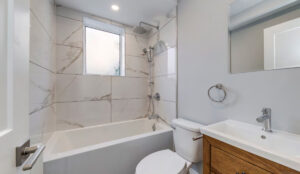 Modern bathroom with tub and shower, marble-style tile walls, and wood vanity