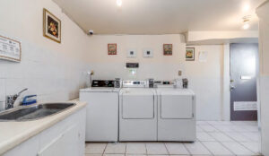 Shared laundry room with washers, dryers, utility sink, and tiled floor